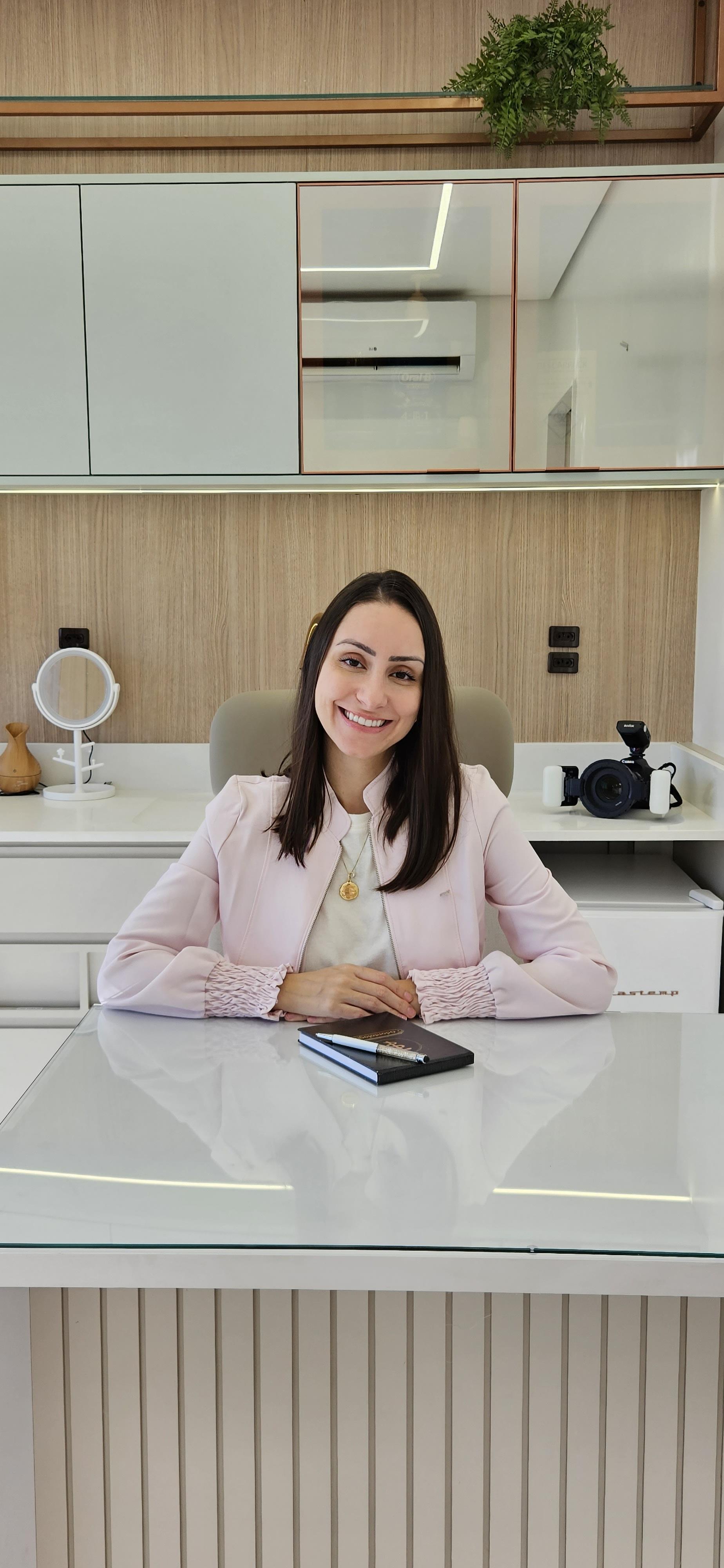 Dentista sorrindo sentada em seu consultório com uma agenda na mesa.