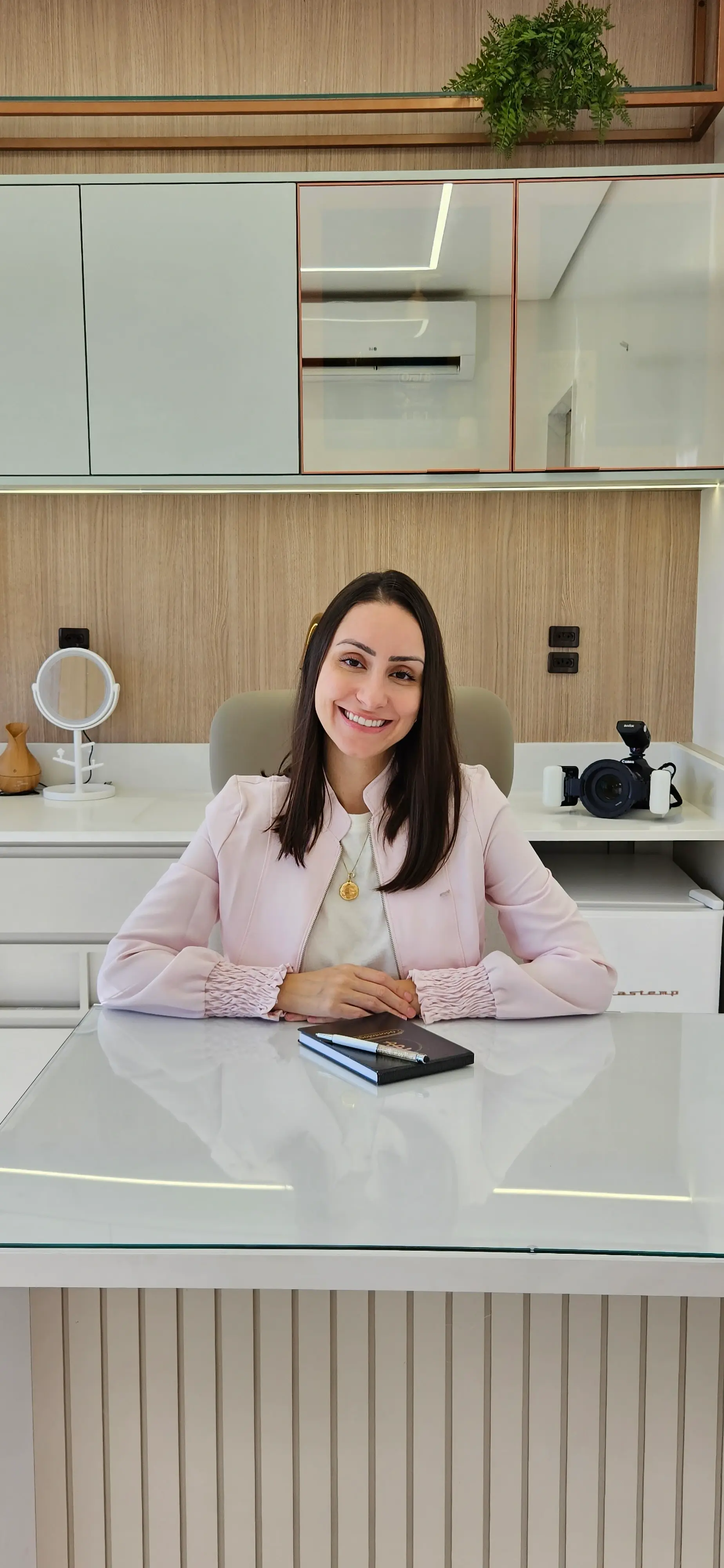 Dentista sorrindo sentada em seu consultório com uma agenda na mesa.