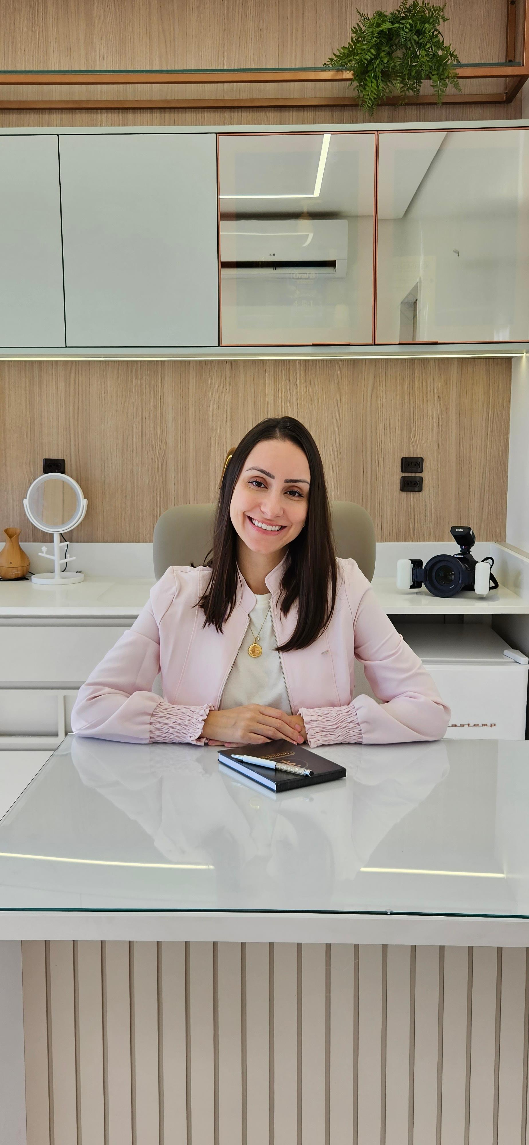 Dentista sorrindo sentada em seu consultório com uma agenda na mesa.